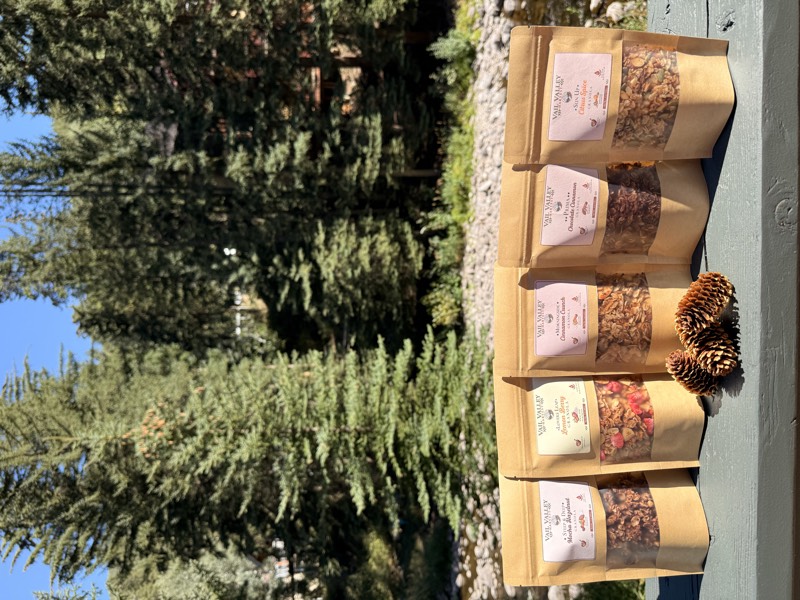 All five Vail Valley Harvest 3 oz pouches fanned on a deck rail with pinecones