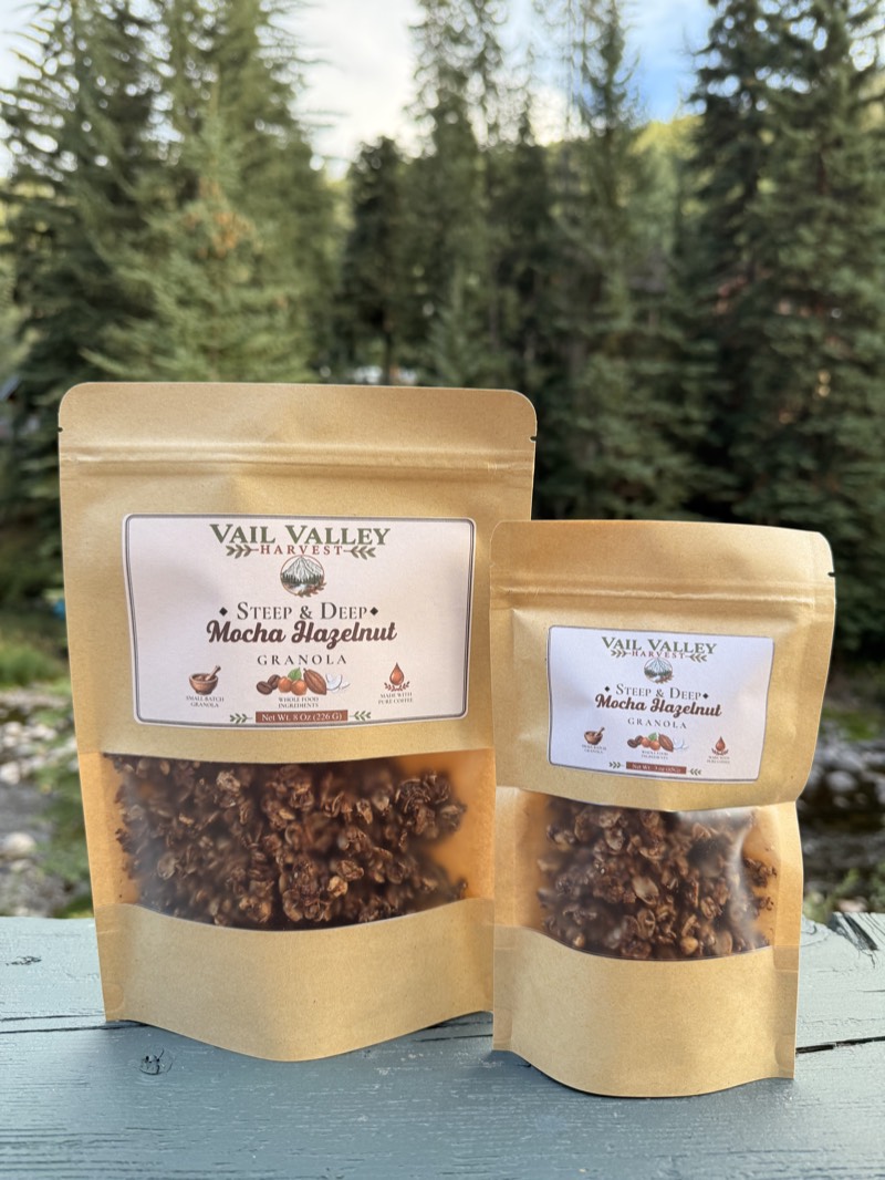 Steep and Deep Mocha Hazelnut granola pouch in front of Vail pines